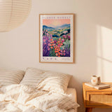 a bedroom scene with a framed poster of a colorful floral landscape hanging on the wall above a bed with striped pillows.