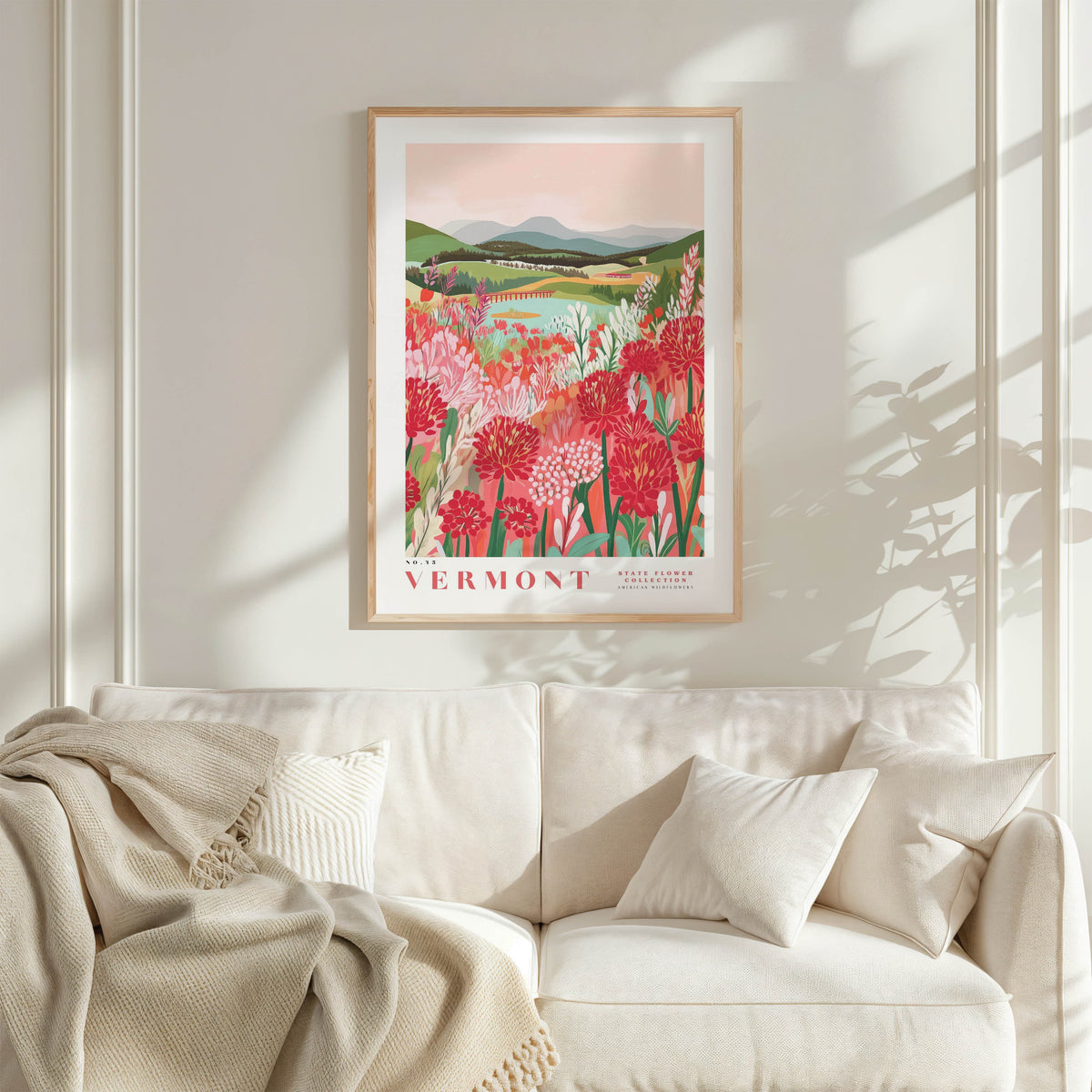 a framed poster of a vibrant floral landscape hanging on a wall above a white couch with a blanket draped over it.