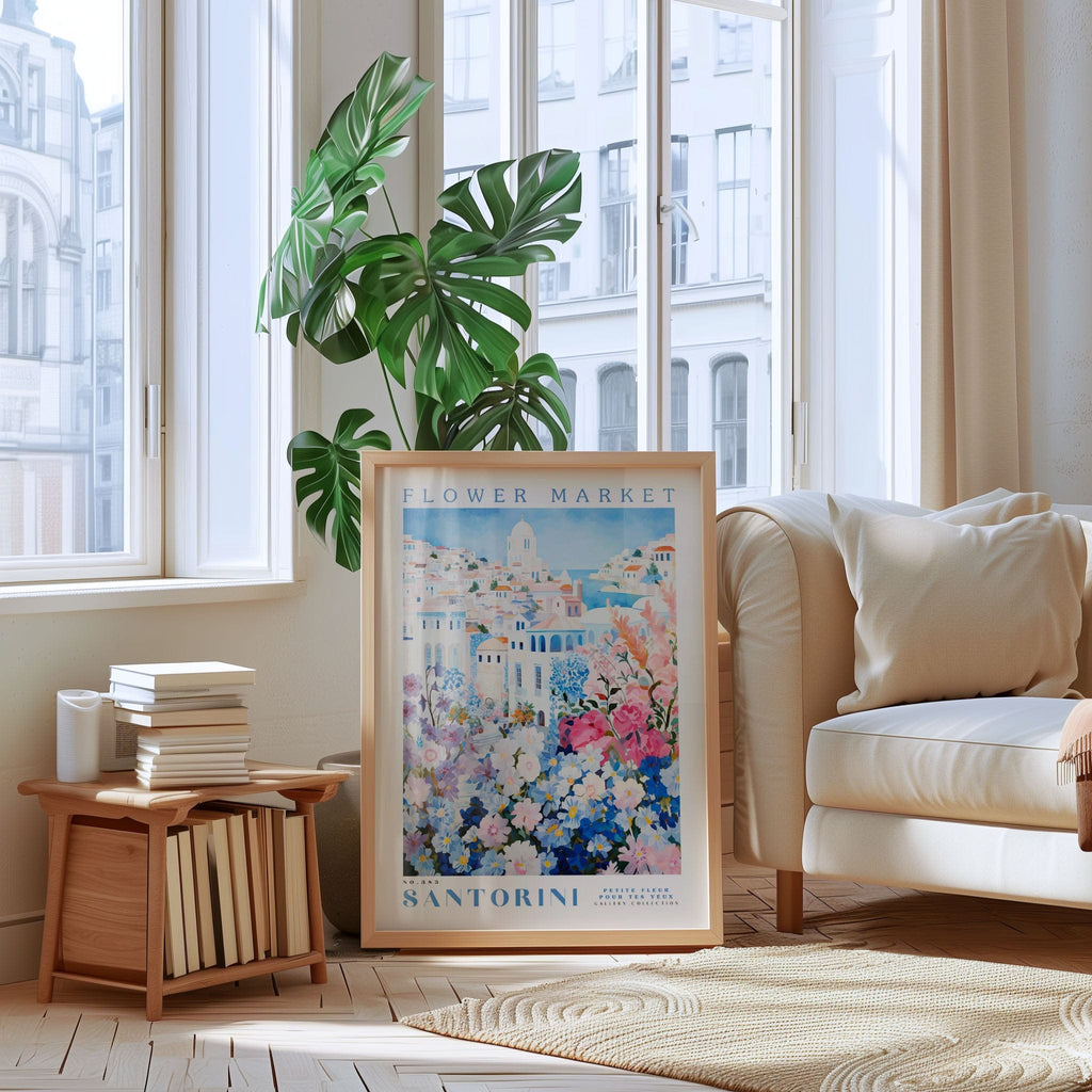 a poster of Santorini's Flower Market, with a large window in the background and a potted plant on the floor.