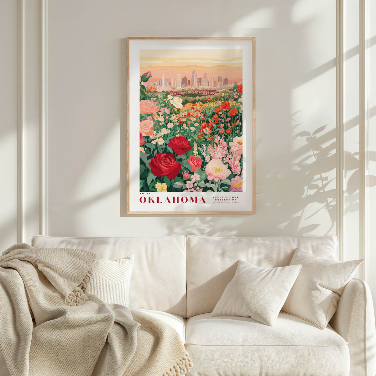 a framed poster of a cityscape with a garden of flowers in the foreground, hanging on a wall above a white couch.