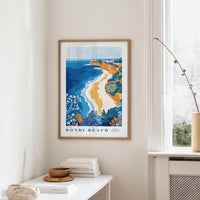 a framed poster of Bondi Beach hanging on a wall, with a white table and a vase of flowers in the foreground.