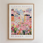 A framed poster depicting a vibrant and colorful cityscape with a variety of flowers and buildings, including a prominent pink flower in the foreground.