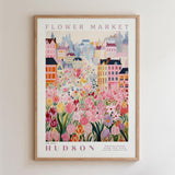 A framed poster depicting a vibrant and colorful cityscape with a variety of flowers and buildings, including a prominent pink flower in the foreground.