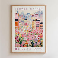 A framed poster depicting a vibrant and colorful cityscape with a variety of flowers and buildings, including a prominent pink flower in the foreground.