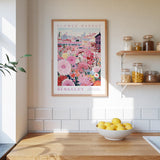 a kitchen scene with a framed poster of a flower market in Berkeley, California, hanging on the wall above a wooden countertop. On the countertop, there is a bowl of lemons and a plant.