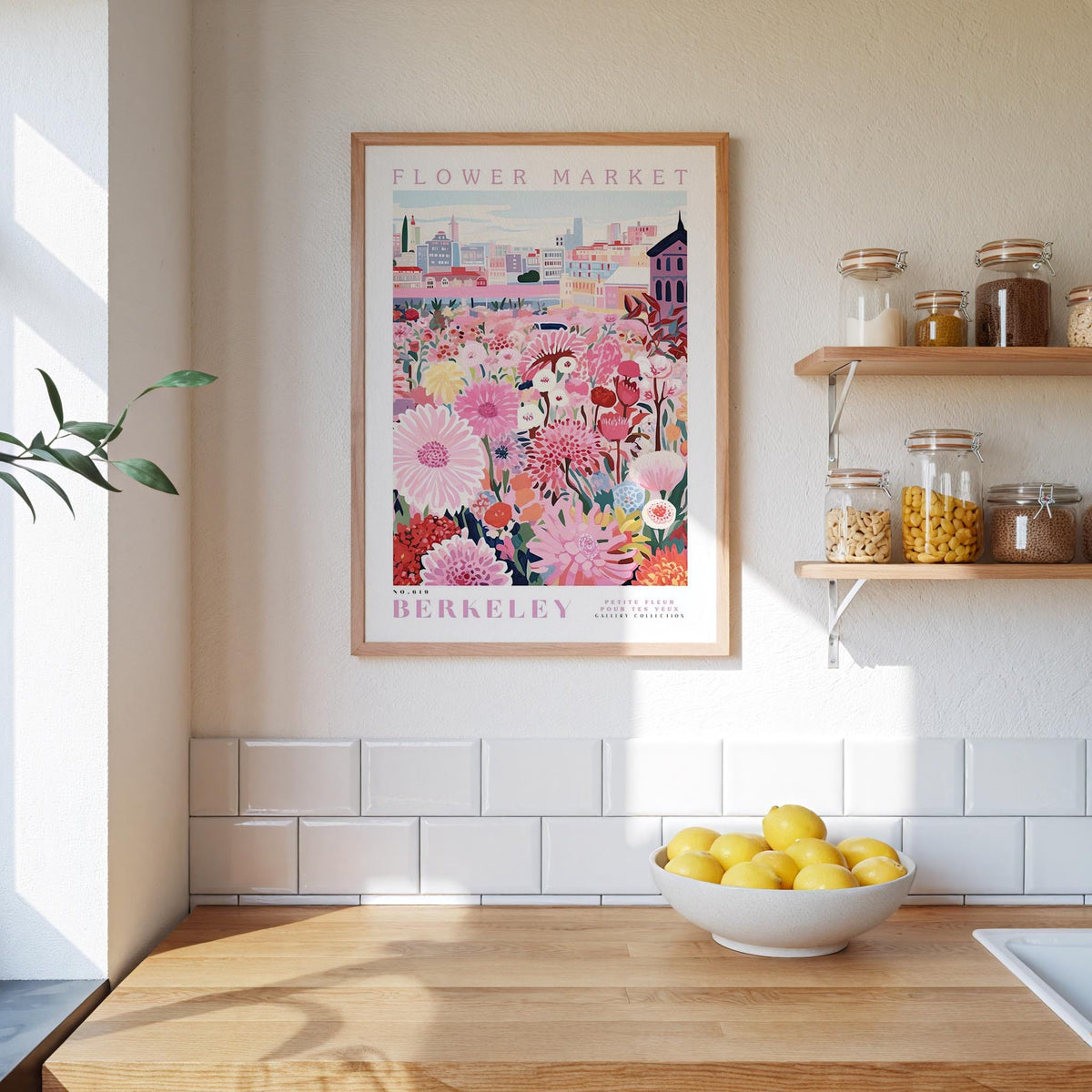a kitchen scene with a framed poster of a flower market in Berkeley, California, hanging on the wall above a wooden countertop. On the countertop, there is a bowl of lemons and a plant.