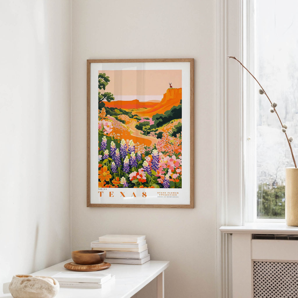 a framed poster of a colorful landscape with flowers hanging on a wall in a room.