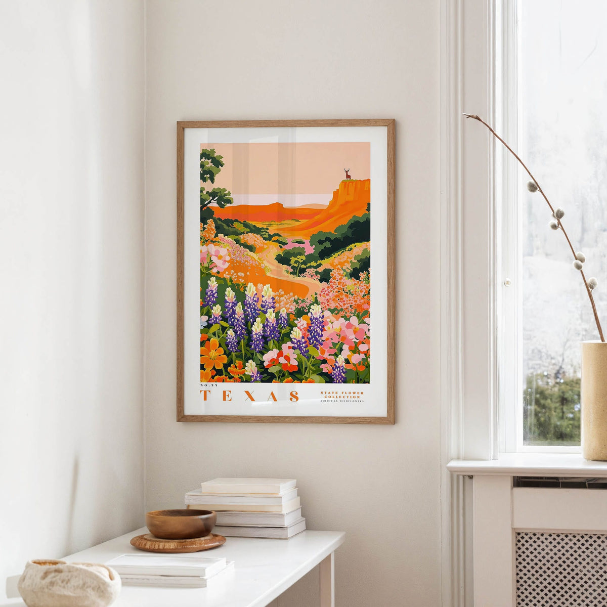 a framed poster of a colorful landscape with flowers hanging on a wall in a room.