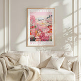 a framed poster of a flower market in Malibu, California, hanging on a wall above a white couch with a blanket draped over it.