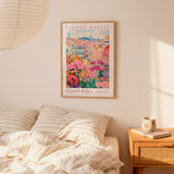 a bedroom setting with a framed poster of a colorful floral scene hanging on the wall above a bed with striped pillows.