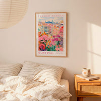 a bedroom setting with a framed poster of a colorful floral scene hanging on the wall above a bed with striped pillows.