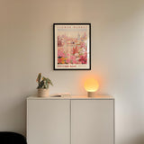 a white cabinet with a potted plant and a lamp on top, set against a wall with a framed poster of a cityscape above it.