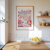 a kitchen scene with a framed poster of a flower market in Krakow hanging on the wall above a wooden counter. On the counter, there is a bowl of lemons and a plant.