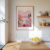 a kitchen scene with a framed poster of a flower market in Macarech, Spain, hanging on the wall above a wooden counter. The poster displays a variety of flowers and plants, creating a vibrant and colorful atmosphere. On the counter, there is a bowl of lemons, adding a touch of freshness to the scene. The kitchen also includes shelves with jars and bottles, as well as a sink, contributing to the overall homey and welcoming ambiance.