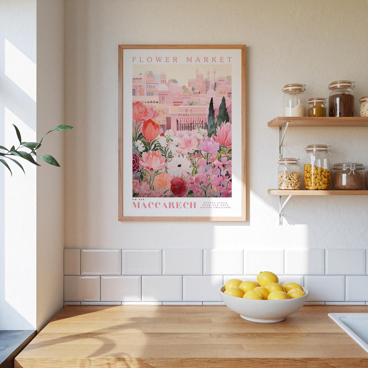a kitchen scene with a framed poster of a flower market in Macarech, Spain, hanging on the wall above a wooden counter. The poster displays a variety of flowers and plants, creating a vibrant and colorful atmosphere. On the counter, there is a bowl of lemons, adding a touch of freshness to the scene. The kitchen also includes shelves with jars and bottles, as well as a sink, contributing to the overall homey and welcoming ambiance.