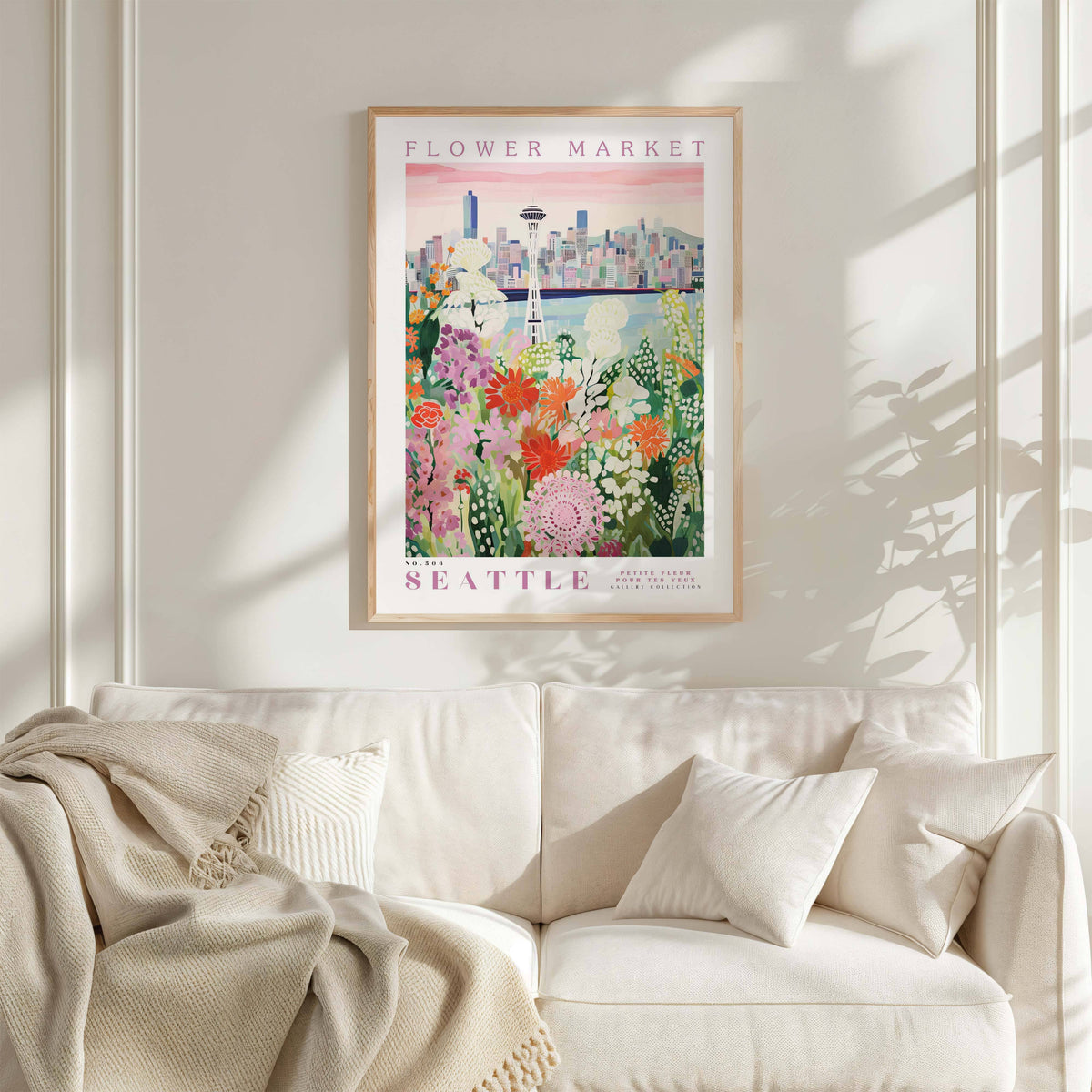 a framed poster of a cityscape with a flower market in the background, hanging on a wall above a white couch with a blanket draped over it.
