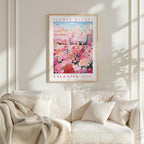 a framed poster of a colorful floral scene hanging on a wall above a white couch with a blanket draped over it.