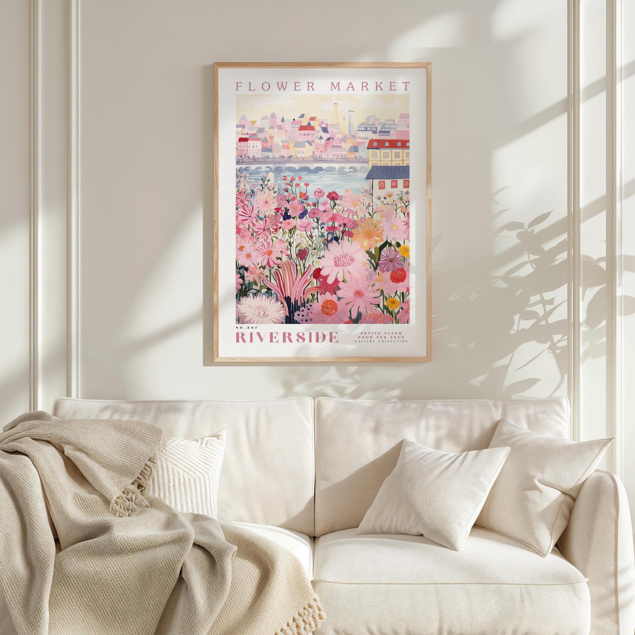 a framed poster of a flower market, with a cityscape in the background, hanging on a wall above a white couch.