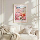 a framed poster of a vibrant floral scene hanging on a wall above a white couch with a blanket draped over it.