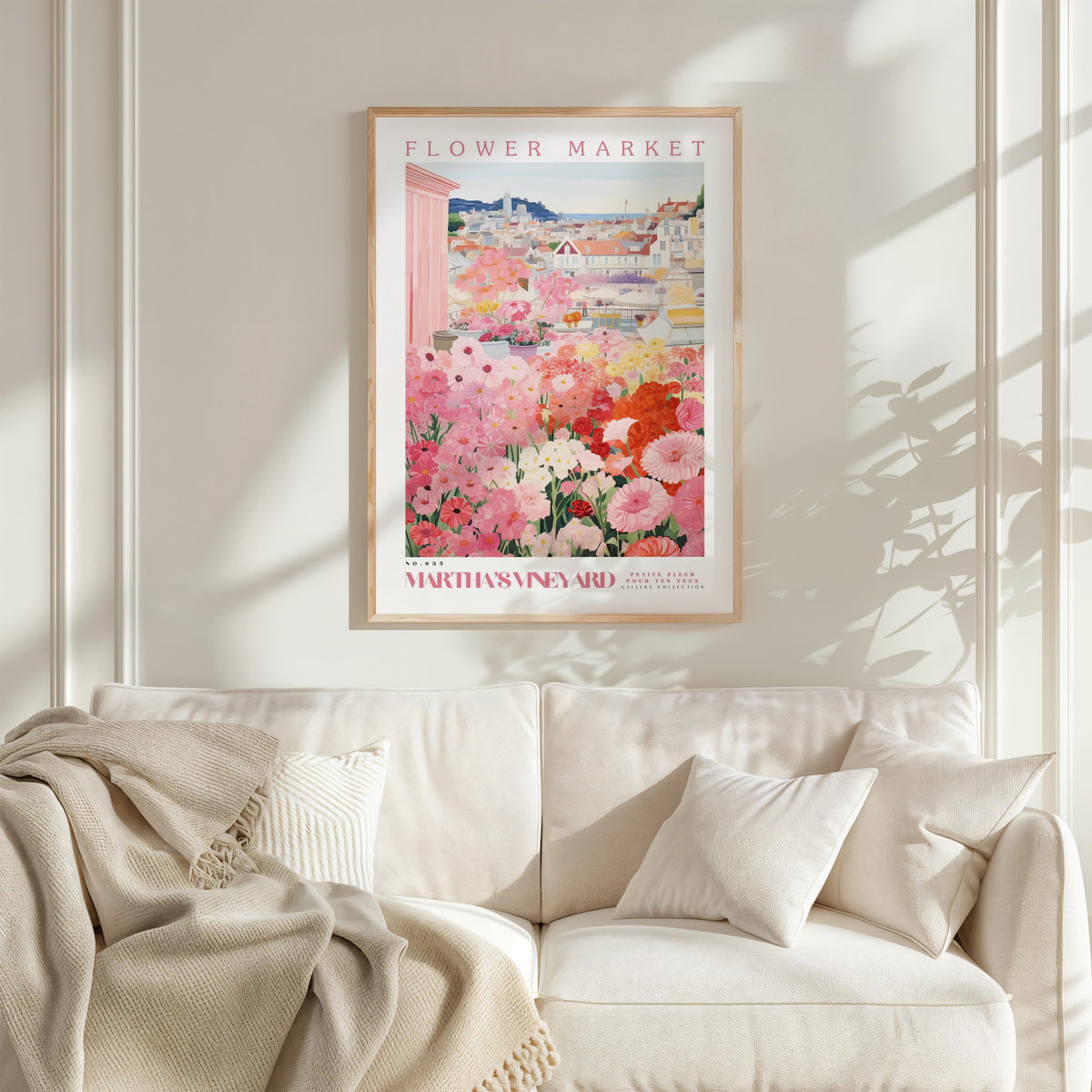 a framed poster of a vibrant floral scene hanging on a wall above a white couch with a blanket draped over it.
