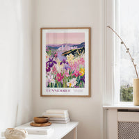 a framed poster of a colorful garden scene with flowers and a cityscape in the background, hanging on a wall in a room.