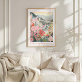 a framed poster of a cityscape with flowers hanging on a wall above a white couch with pillows.