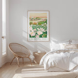 A bedroom with a large framed poster of a field of flowers hanging on the wall, a woven chair, and a bed with white bedding.