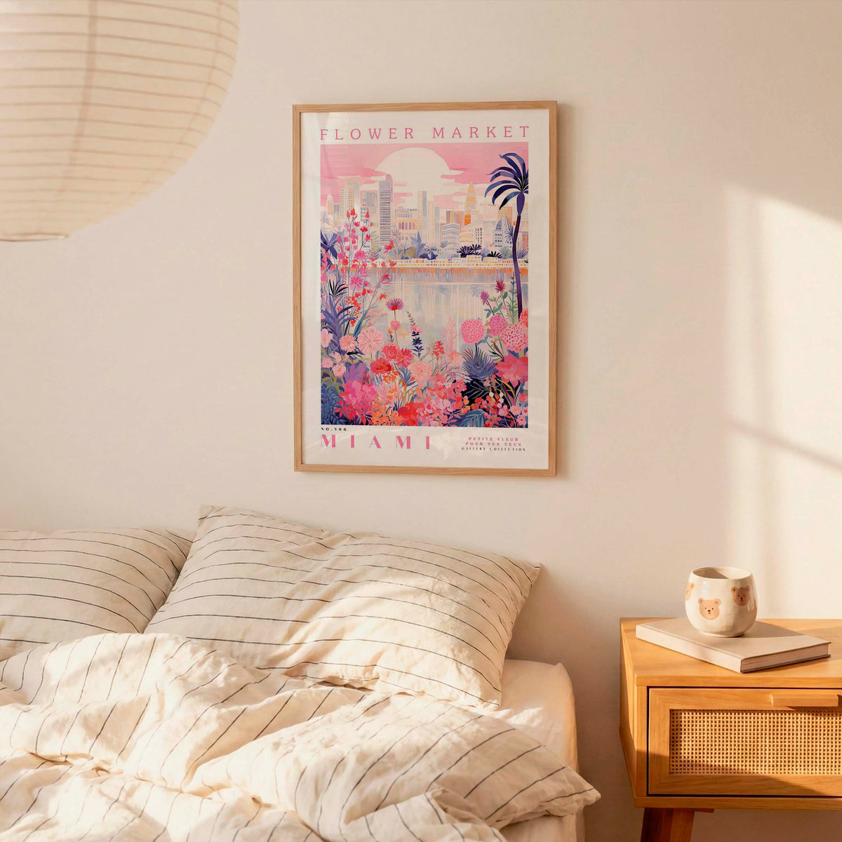 a bedroom scene with a framed poster of a cityscape and flowers hanging on the wall above a bed with striped pillows.