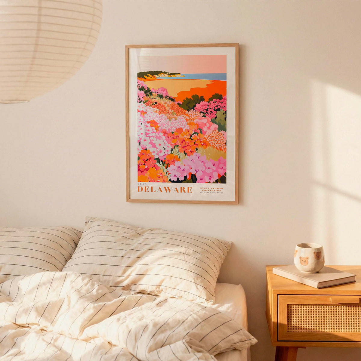 a bedroom scene with a framed poster of a colorful floral landscape hanging on the wall above a bed with striped pillows.
