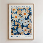 The image is a framed poster or artwork featuring a vibrant floral pattern in shades of blue, white, and orange. The text on the poster reads "FLOWER MARKET" and "DUBAI", indicating the subject of the artwork is the flower market in Dubai.