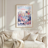 a framed poster of a cityscape with flowers, hanging on a wall above a white couch with pillows.