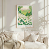 a framed poster of a field of flowers hanging on a wall above a white couch with a blanket draped over it.
