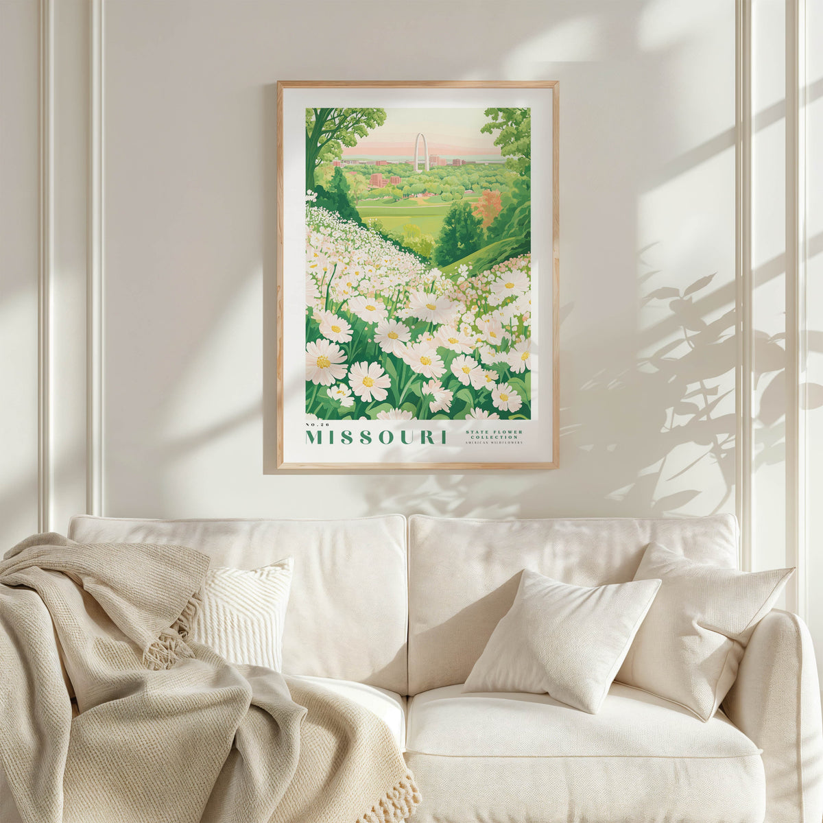 a framed poster of a field of flowers hanging on a wall above a white couch with a blanket draped over it.