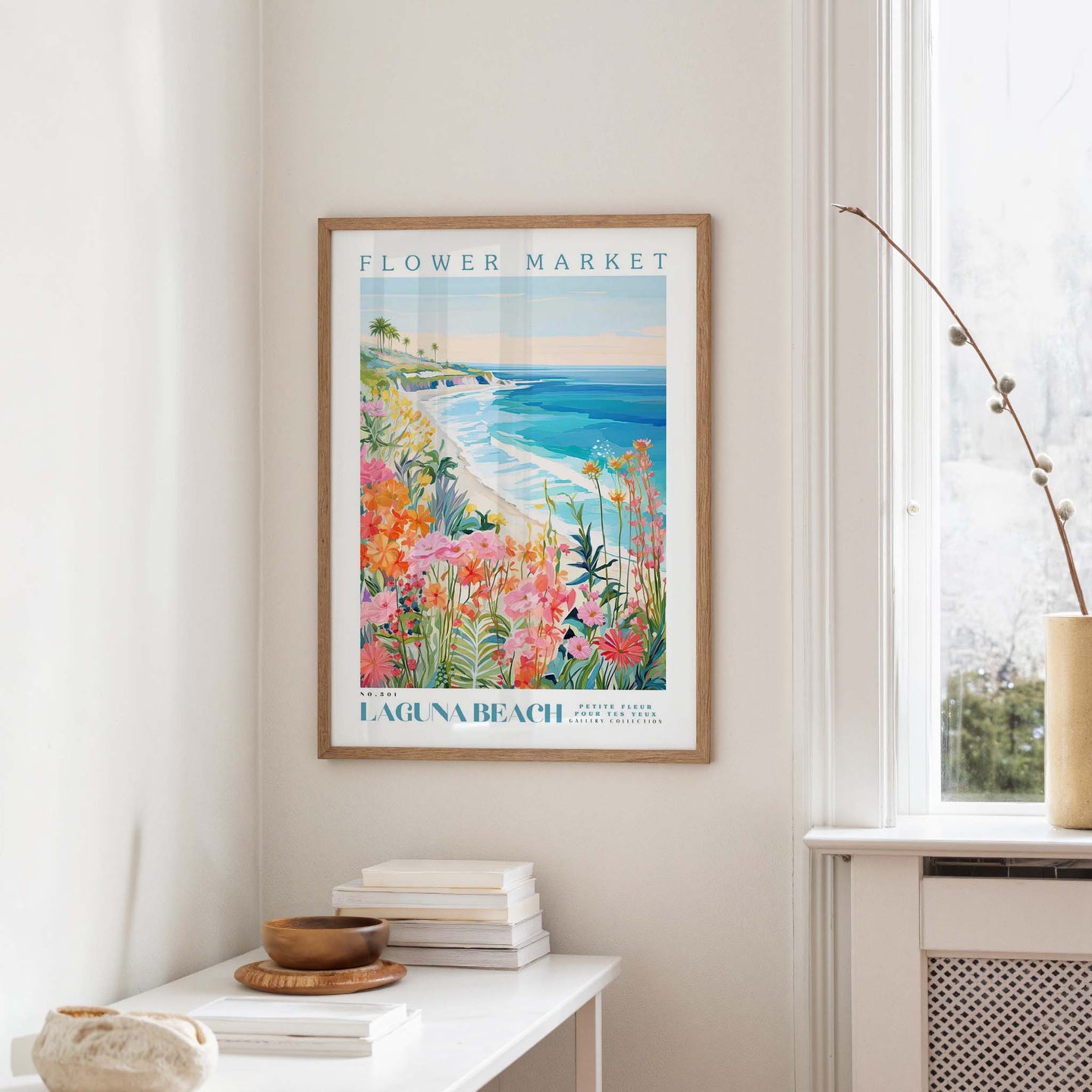 a framed poster of a beach scene with a colorful, tropical landscape, hanging on a wall in a room with a white table and a vase of flowers.