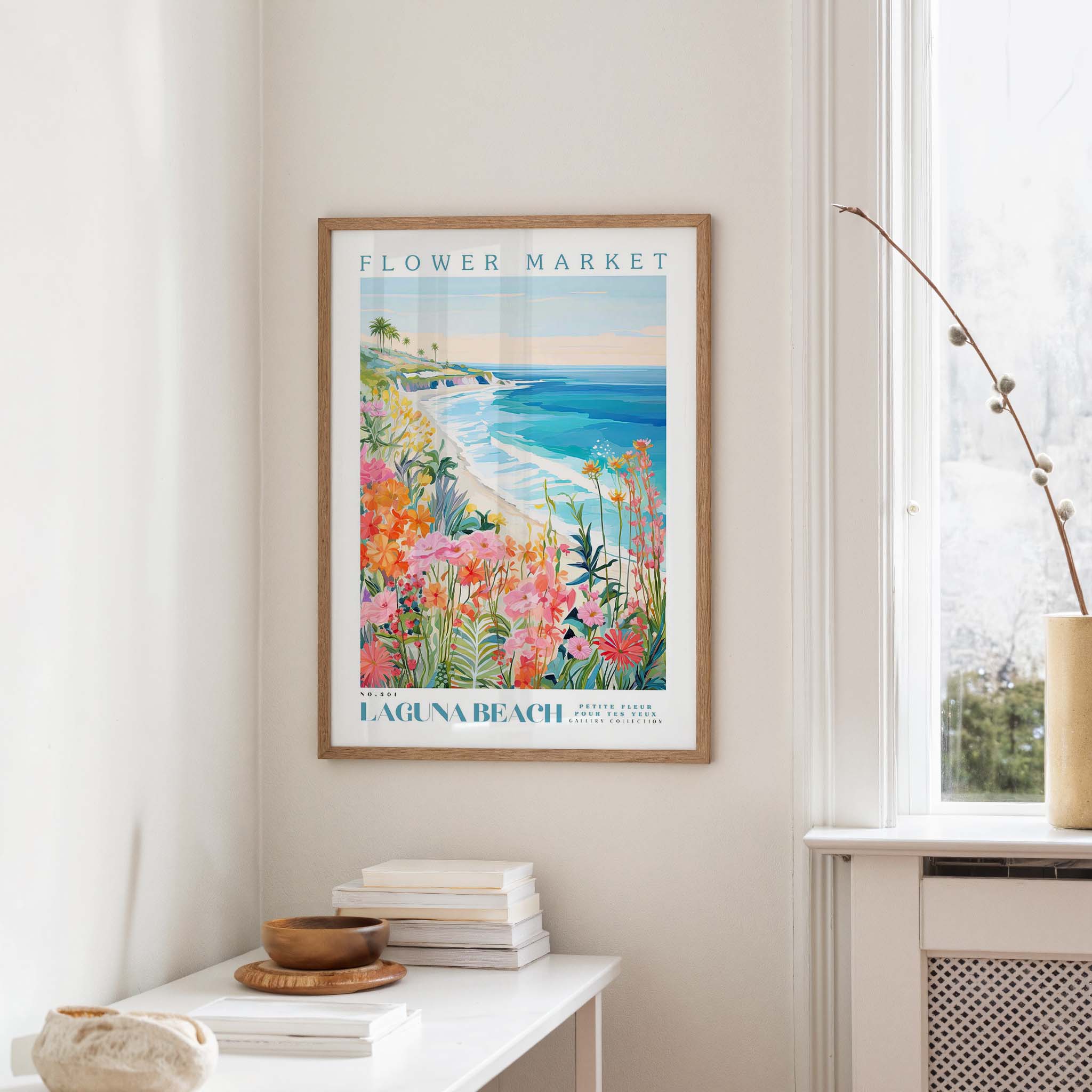 a framed poster of a beach scene with a colorful, tropical landscape, hanging on a wall in a room with a white table and a vase of flowers.