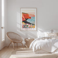 a serene bedroom scene with a large bed, a woven chair, and a framed poster of a coastal landscape hanging on the wall.