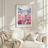 a framed poster of a flower market in Missoula, Montana, hanging on a wall above a white couch.