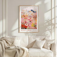 a framed poster of a colorful floral scene hanging on a wall above a white couch with pillows.