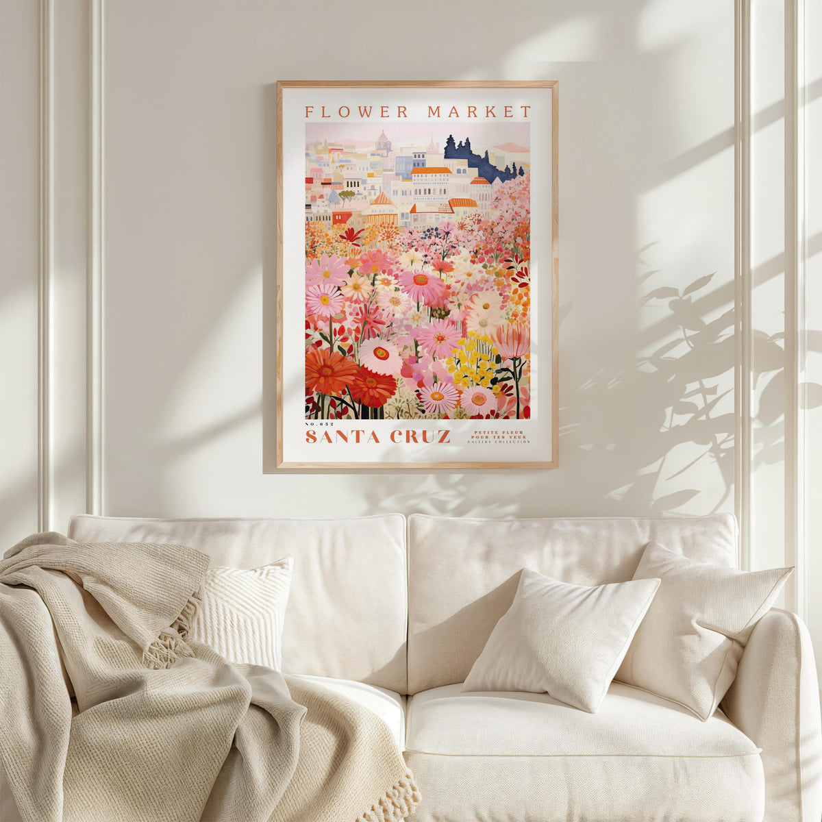 a framed poster of a colorful floral scene hanging on a wall above a white couch with pillows.