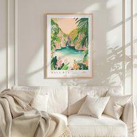 a framed poster of a tropical beach scene with palm trees, flowers, and a turquoise ocean, hanging on a white wall above a white couch with pillows.