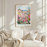 a framed poster of a colorful garden scene hanging on a wall above a white couch.