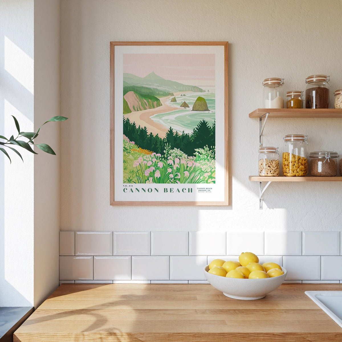 a kitchen counter with a bowl of lemons, a framed poster of a coastal landscape, and a shelf with jars and bottles.