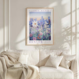 a framed poster of a cityscape with flowers hanging on a wall above a white couch with pillows.