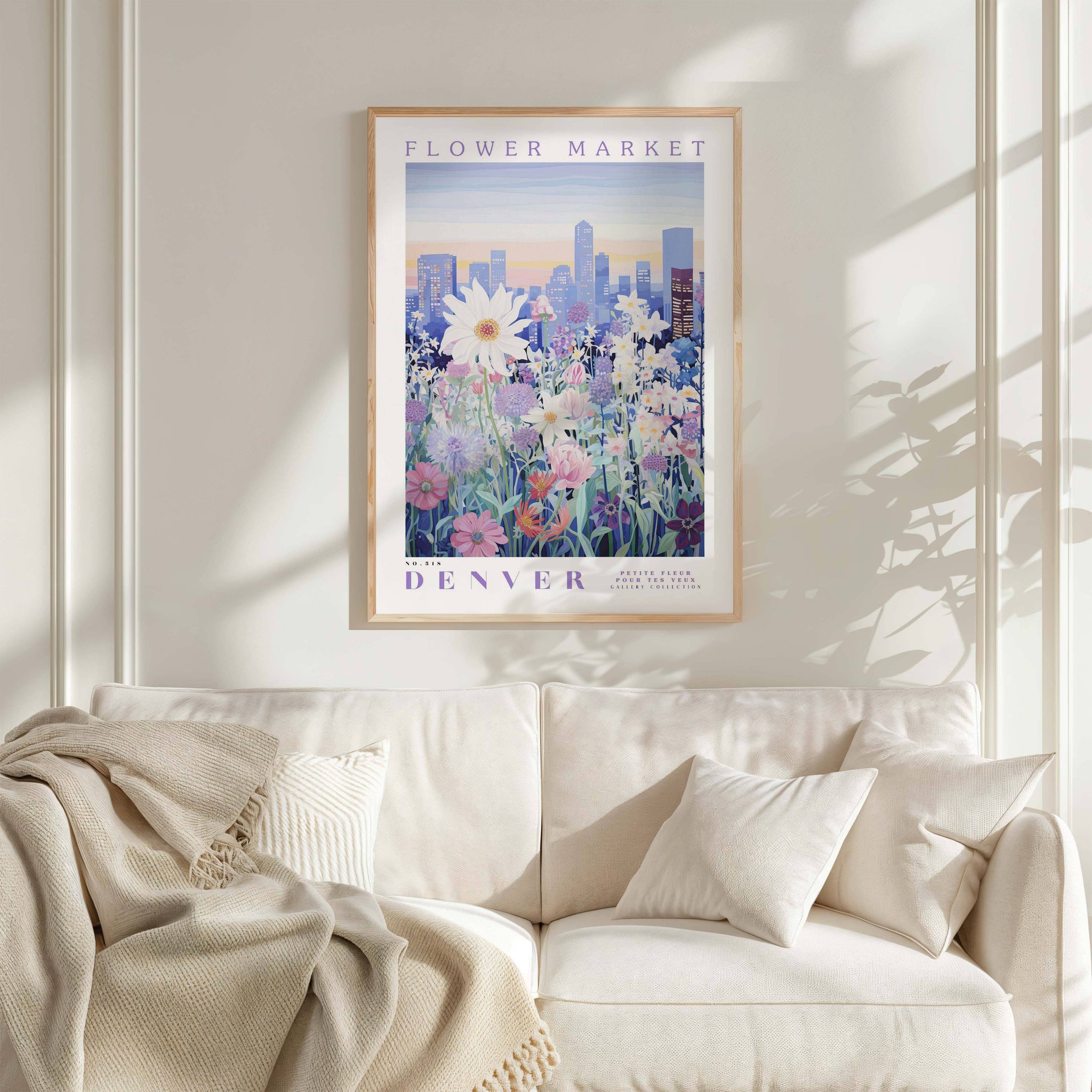 a framed poster of a cityscape with flowers hanging on a wall above a white couch with pillows.