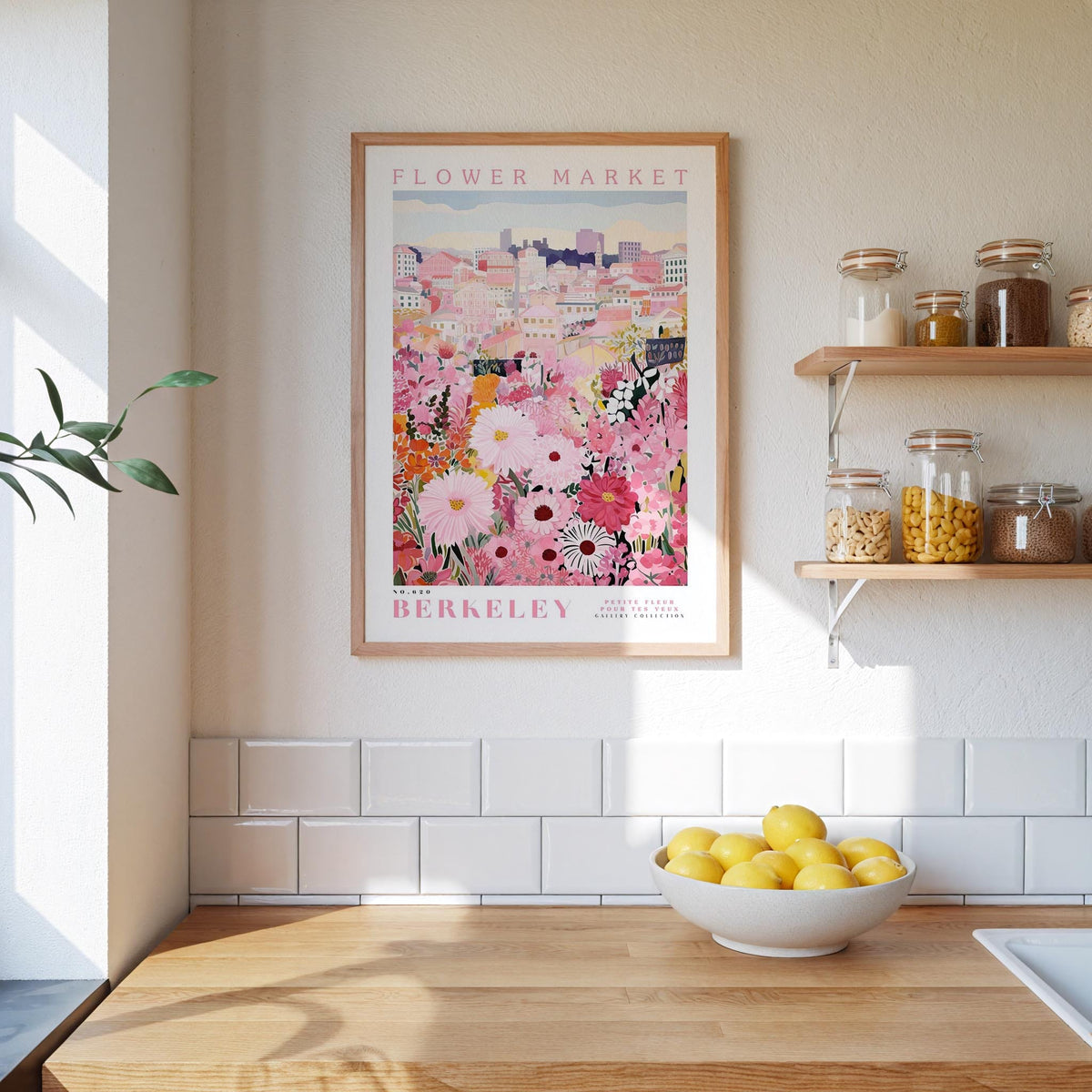 a kitchen counter with a bowl of lemons, a framed poster of a flower market, and shelves with jars and containers.