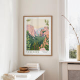 a framed poster of Yosemite National Park hanging on a wall, with a white table and a vase of flowers in the foreground.