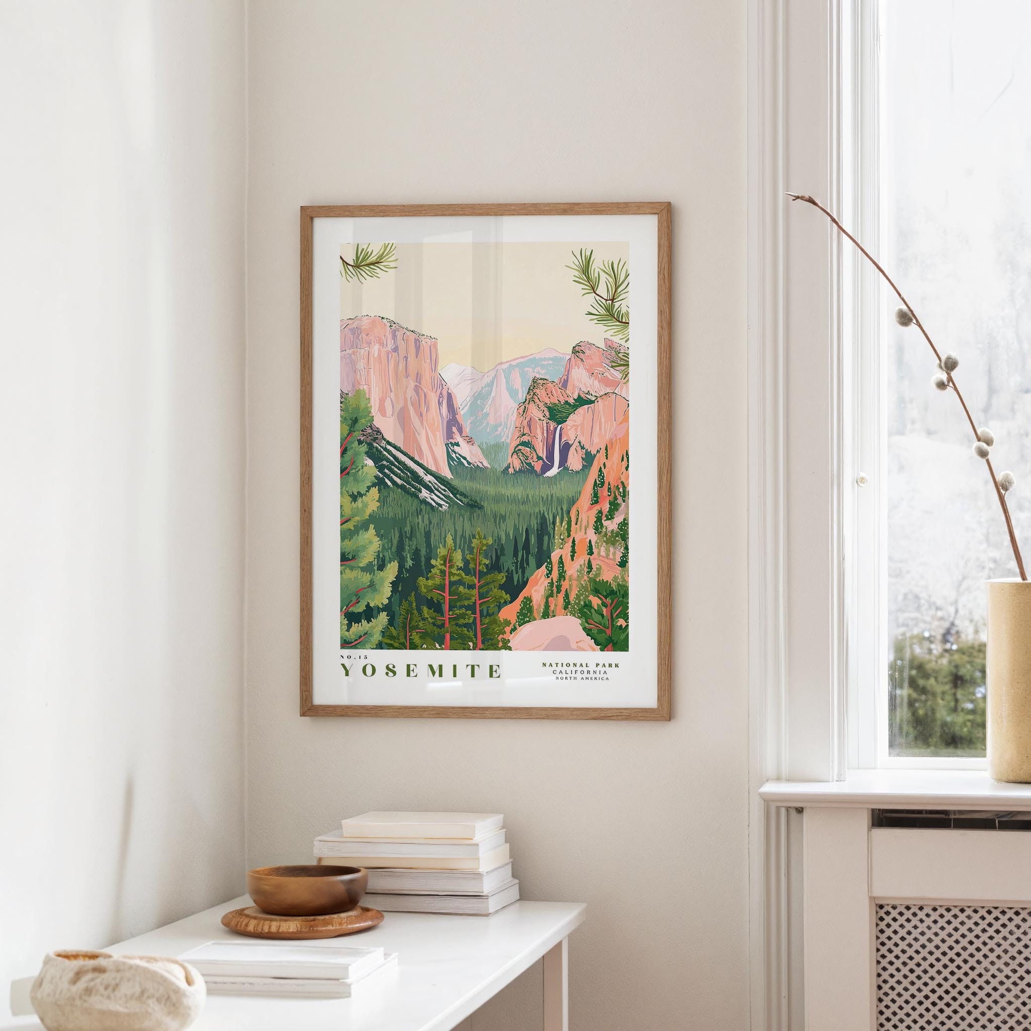a framed poster of Yosemite National Park hanging on a wall, with a white table and a vase of flowers in the foreground.