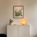 a framed poster of Yosemite National Park hanging on a wall above a white cabinet with a plant and a lamp on top.