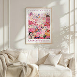 a framed poster of a colorful floral scene hanging on a wall above a white couch with a blanket draped over it.