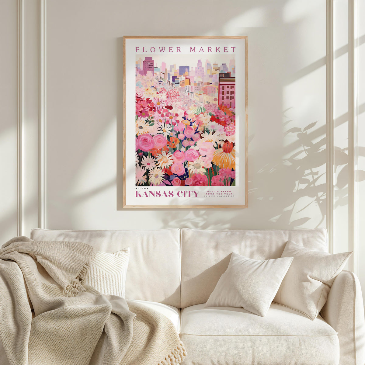 a framed poster of a colorful floral scene hanging on a wall above a white couch with a blanket draped over it.